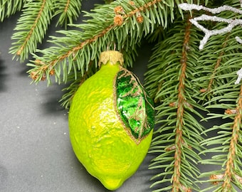 Op de afbeelding: Een groene glazen kerstbal in de vorm van een limoen met een groen blad en gouden glitteraccenten.