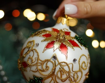 May include: White Christmas ornament with gold and red floral designs and glitter accents.