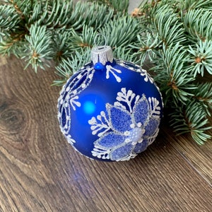May include: A blue Christmas ornament with a white snowflake design. The ornament is made of glass and has a shiny finish.
