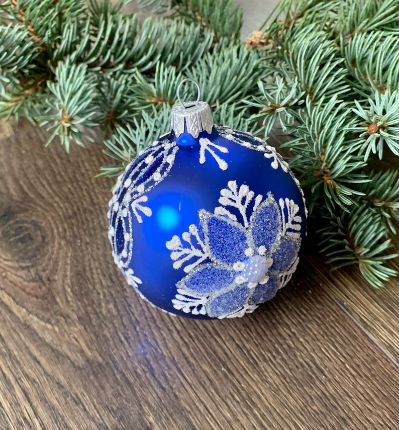 May include: A blue Christmas ornament with a white snowflake design. The ornament is made of glass and has a shiny finish.