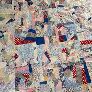 May include: A patchwork quilt constructed from a multitude of fabric scraps in various colors and patterns, including red polka dots, blue florals, stripes, and solid blocks. The textile features a chaotic, multi-colored design of stitched squares.