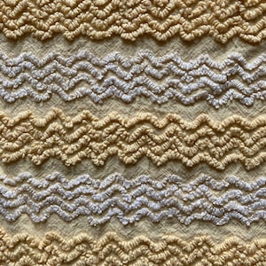 May include: A close-up of a yellow and white fabric with a wavy pattern. The fabric is textured and has a soft, fluffy appearance.