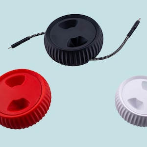 Może przedstawiać: Trzy organizatory kabli w kolorze czarnym, czerwonym i białym. Każdy organizer ma okrągły kształt z żebrowanym wzorem i dwoma wycięciami w środku.