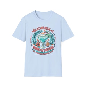 Può includere: Una t-shirt azzurro chiaro con una stampa grafica di un bicchiere da margarita con una fetta di lime e un ombrellino. Il testo recita VACATION RULE #1: MOMMY NEEDS A MARGARITA, circondato da foglie di palma tropicali e fiori di ibisco color corallo e ottanio.