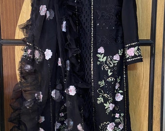 May include: A black embroidered dress with a sheer overlay and floral details. The dress has a ruffled neckline and long sleeves.