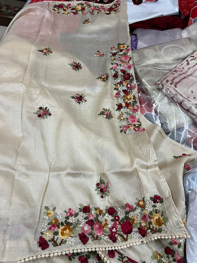 May include: A cream-colored silk scarf with intricate floral embroidery in shades of red, pink, and yellow. The scarf has a delicate white lace trim.