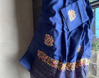May include: A dark blue silk saree with intricate floral embroidery in shades of pink, yellow, and green. The saree has a beaded border and a matching blouse piece.