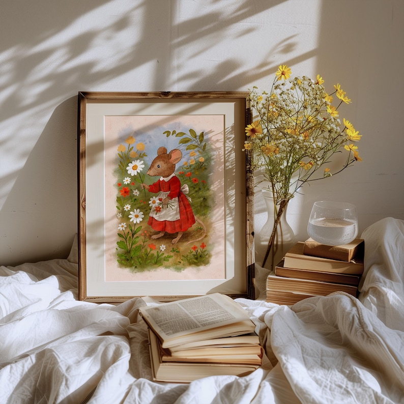 May include: A framed art print featuring a whimsical illustration of a mouse in a red dress and white apron, picking flowers in a garden. The artwork is set against a soft, pastel background, framed in a wooden frame. A vase of yellow flowers and a stack of books are also visible.