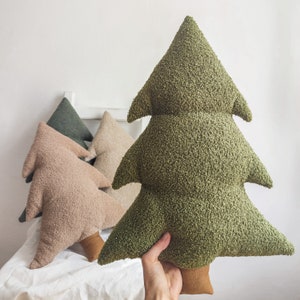 Könnte beinhalten: Drei Plüschkissen in Form von Weihnachtsbäumen. Das größte Kissen ist grün, das mittlere Kissen ist beige und das kleinste Kissen ist grün. Die Kissen sind auf einer weißen Oberfläche angeordnet.