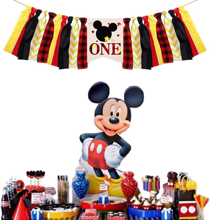 Puede incluir: Un conjunto de decoraci&oacute;n para una fiesta de primer cumplea&ntilde;os con tem&aacute;tica de Mickey Mouse. El conjunto incluye una pancarta con tela de cuadros rojos y negros, tela de chevron amarilla y blanca y tela negra con lunares amarillos. La pancarta tambi&eacute;n incluye una gran cabeza de Mickey Mouse con orejas negras y una cara blanca. La pancarta dice "ONE" en letras blancas. El conjunto tambi&eacute;n incluye un recorte de cart&oacute;n de Mickey Mouse, una mesa con varias decoraciones de fiesta y una variedad de golosinas.
