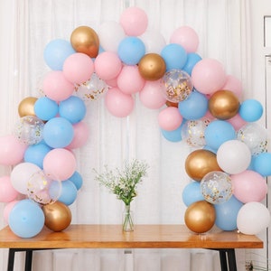 May include: A balloon arch made of pink, blue, white, and gold balloons. The balloons are arranged in a cascading pattern, creating a festive and celebratory atmosphere.