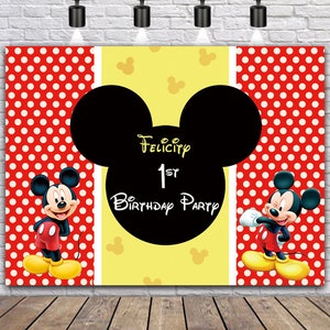 May include: A red and yellow Mickey Mouse themed birthday party backdrop with white polka dots. The backdrop features a large black Mickey Mouse head with the text "Felicity 1st Birthday Party".