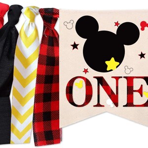 Puede incluir: Una pancarta de cuadros rojos y negros con una silueta negra de la cabeza de Mickey Mouse y la palabra "ONE" en letras negras. La pancarta tiene estrellas amarillas y orejas de Mickey Mouse.