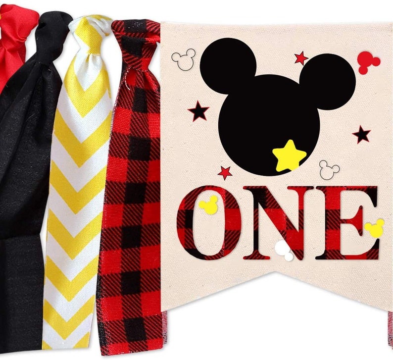 Puede incluir: Una pancarta de cuadros rojos y negros con una silueta negra de la cabeza de Mickey Mouse y la palabra "ONE" en letras negras. La pancarta tiene estrellas amarillas y orejas de Mickey Mouse.