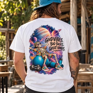 May include: A white t-shirt featuring a graphic of a skeleton wearing a floral shirt, shorts, and sunglasses, sitting on a blue exercise ball. The design includes planets, stars, and the text: GOOD VIBES. BAD BACKS. GREAT HANDS.