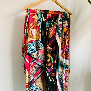 May include: Four colourful silk scarves with different patterns hanging on a wooden hanger. The scarves are in shades of pink, blue, green, yellow, and black.