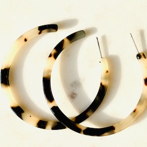 May include: A pair of large hoop earrings made of tortoiseshell-patterned plastic. The earrings are a light brown colour with dark brown and black accents.
