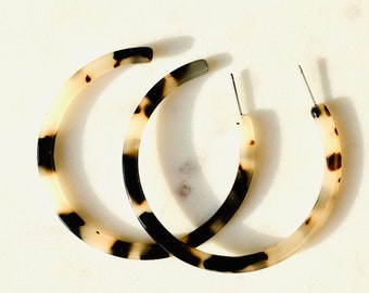 May include: A pair of large hoop earrings made of tortoiseshell-patterned plastic. The earrings are a light brown color with dark brown and black accents.