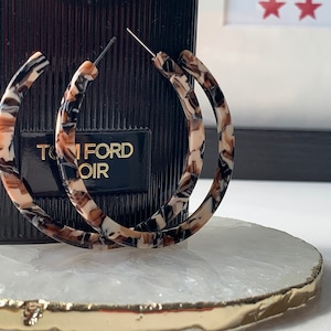 May include: A pair of large hoop earrings with a brown, black, and white marbled pattern.