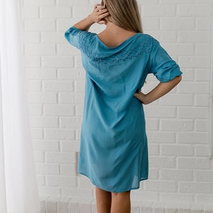 May include: A light blue, knee-length dress with a decorative neckline featuring a beaded design. The dress has a relaxed fit and three-quarter sleeves.