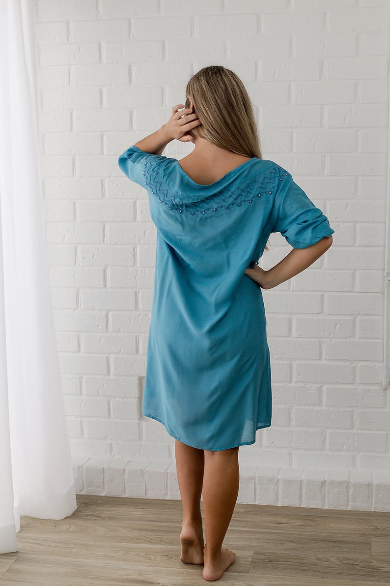 May include: A light blue, knee-length dress with a decorative neckline featuring a beaded design. The dress has a relaxed fit and three-quarter sleeves.