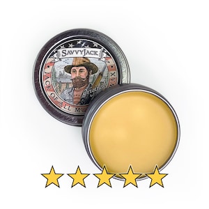 Puede incluir: Una lata de cera Savvy Jack Original con un bálsamo amarillo claro. La tapa de la lata presenta un retrato de un hombre con barba y sombrero, con el texto "Savvy Jack" y "Jack of All Muds Wax".