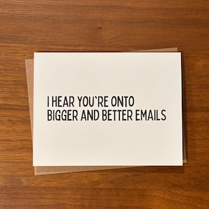 May include: A white rectangular greeting card with black text that reads I HEAR YOU'RE ONTO BIGGER AND BETTER EMAILS, layered on top of a brown kraft paper envelope. The card features a clean, simple design with bold, sans-serif typography.
