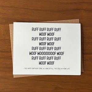 May include: A white greeting card with black text on a brown envelope. The card features the phrase "RUFF RUFF RUFF RUFF WOOF WOOF" repeated multiple times. The text at the bottom reads "- THE HAPPY BIRTHDAY SONG, AS SUNG BY ALL THE DOGS IN YOUR LIFE."
