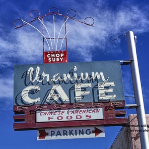May include: A vintage neon sign for a restaurant called "Uranium Cafe" with the words "Chinese & American Foods" and "Parking" below. The sign is red, white, and blue with a red box at the top that says "Chop Suey".