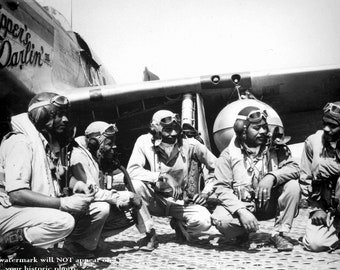 May include: Four men in military uniforms stand in front of a black and white P-51 Mustang fighter plane. The plane has the words "Skipper's Darlin'" painted on the side. The men are wearing aviator goggles and helmets.