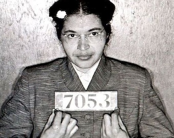 May include: Black and white photo of a woman wearing glasses and a striped jacket. She is holding a white card with the number "705.3" printed on it.