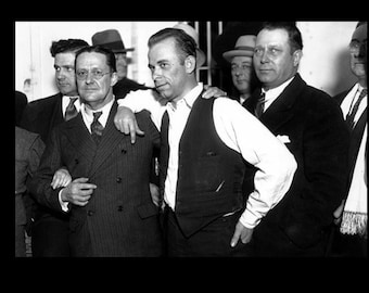 May include: Black and white photo of a group of men in suits and hats. The men are standing together and looking at the camera. The man in the center is wearing a vest and has his arm around the man to his right.