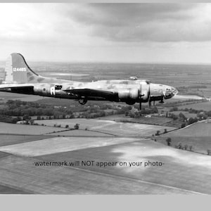 Puede incluir: Una fotografía en blanco y negro de un bombardero B-17 volando sobre un campo. El avión está en vuelo y el número de cola "124485" es visible en la cola.
