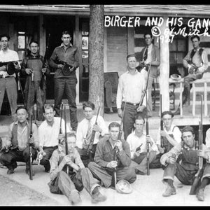 Peut inclure: Une photographie en noir et blanc d'un groupe d'hommes posant avec des fusils. Les hommes sont debout et assis sur un porche. L'enseigne au-dessus d'eux indique "Birger and His Gang" avec la signature "O.K. Mitchell 1927".