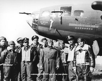 May include: Black and white photograph of a group of airmen posing in front of a B-17 bomber. The aircraft is labeled "MEMPHIS BELLE" with a pin-up girl graphic. The plane has several swastika symbols painted on it.