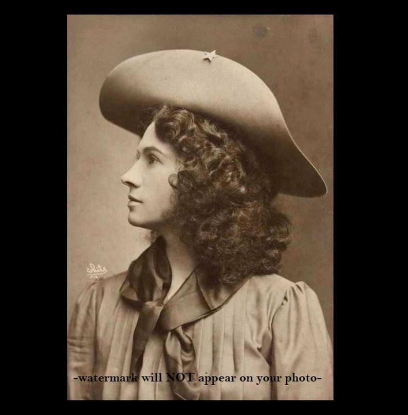 May include: A sepia-toned portrait of a woman with curly hair wearing a wide-brimmed hat with a star on the front. She is wearing a collared shirt with a bow tie.