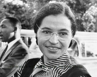 May include: Black and white photo of a woman wearing glasses and a striped shirt, smiling. A man is standing behind her, partially out of frame.