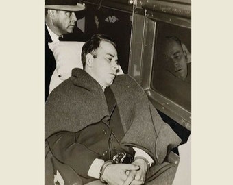 May include: A black and white photo of a man in handcuffs, wearing a coat and sitting in a vehicle. He is being escorted by another man wearing a hat.