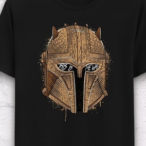 May include: Black t-shirt with a brown and gold illustration of a Mandalorian helmet. The helmet has the words "This is the way" written across the visor.