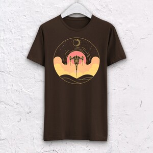 May include: A brown t-shirt with a graphic of a spaceship flying through a sunset with a crescent moon in the sky.