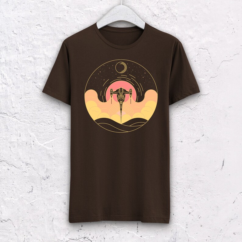May include: A brown t-shirt with a graphic of a spaceship flying through a sunset with a crescent moon in the sky.