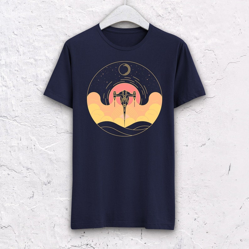 May include: A navy blue t-shirt with a graphic of a spaceship flying through a sunset with a crescent moon in the background.