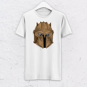 May include: White t-shirt with a brown illustration of a Mandalorian helmet. The helmet has the words "This is the way" written on it.