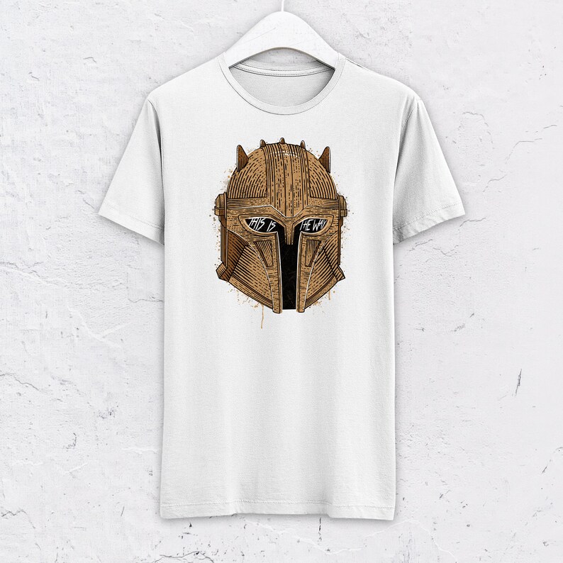 May include: White t-shirt with a brown illustration of a Mandalorian helmet. The helmet has the words "This is the way" written on it.