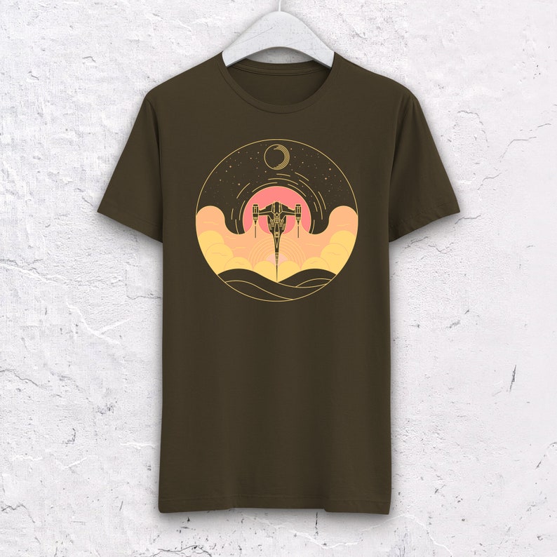 May include: A brown t-shirt with a graphic of a spaceship flying through a sunset with a crescent moon in the background.