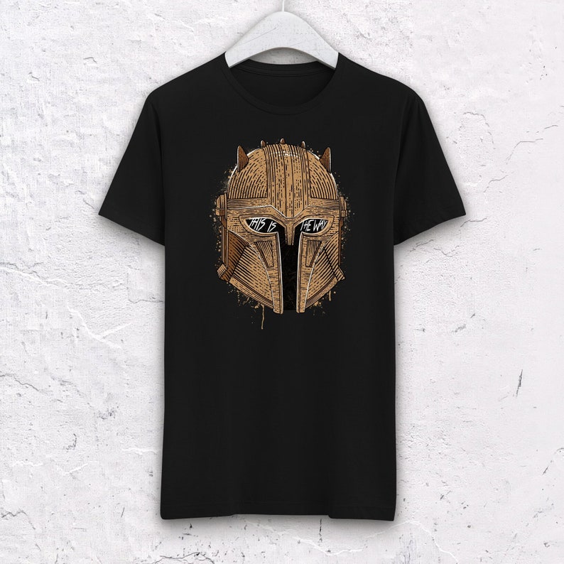 May include: Black t-shirt with a brown and gold illustration of a Mandalorian helmet. The helmet has the words "This is the way" written across the visor.