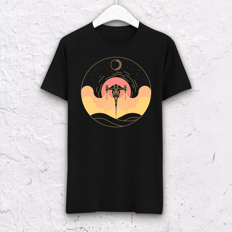 May include: Black t-shirt with a gold and orange graphic of a spaceship flying through a starry sky with a crescent moon.