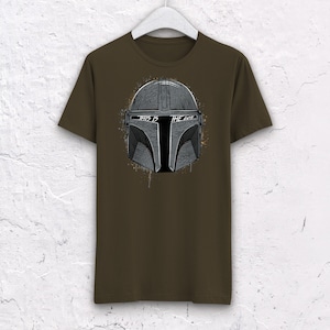 May include: A brown t-shirt with a gray and black graphic of a Mandalorian helmet. The text "This is the Way" is printed on the helmet.