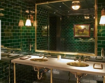 May include: A bathroom with green tile walls and a large mirror with a gold frame. The bathroom has two sinks with gold faucets and a white countertop. There is a small picture of a horse on the wall above the mirror.