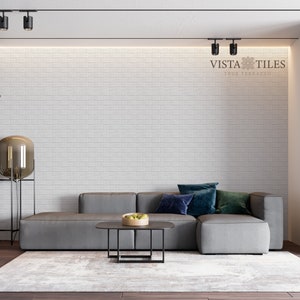 May include: A gray sectional sofa with blue and green throw pillows sits in front of a white brick wall. The room has a modern design with track lighting and a black bookshelf.